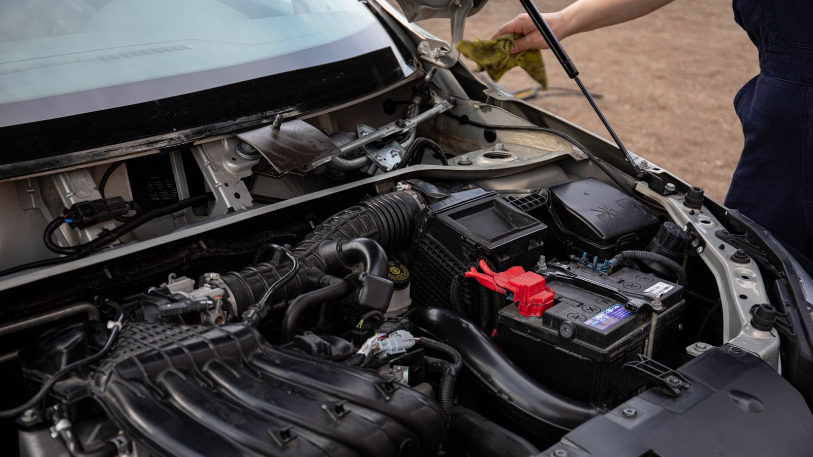 A mechanic checking the engine bay and battery of a car with the hood up.